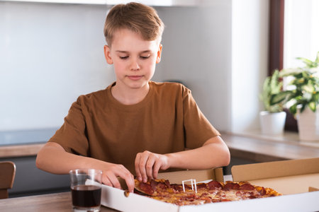 A teenager tears off a piece of pizza in the kitchen at home. Food delivery.の写真素材