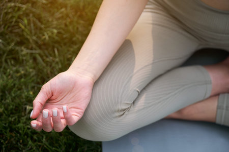 Close-up of a womans hands on a background of green grass. Young woman doing yoga in the park at...