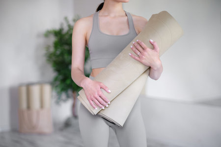Young woman holding yoga mats while standing in a light studio.