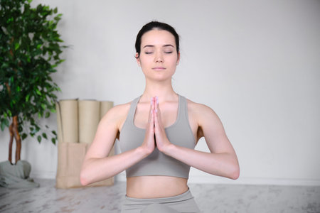 Portrait of a young woman who meditates in the studio while sitting in a half lotus position on a yoga mat.の写真素材