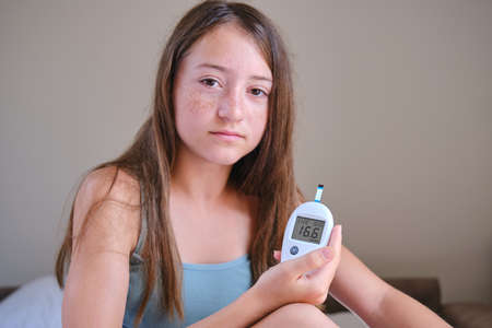 A teenage girl shows the screen of a glucometer with the results of a blood test for diabetes into the camera.の写真素材