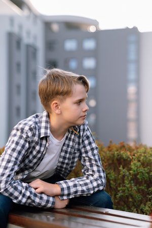 Stylish teenager in casual clothes is relaxing outdoors sitting on a park bench.の写真素材