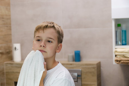Reflection of schoolboy wiping his face with a towel after washing in bathroom.の写真素材