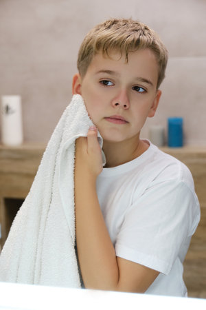Reflection of schoolboy wiping his face with a towel after washing in bathroom.の写真素材