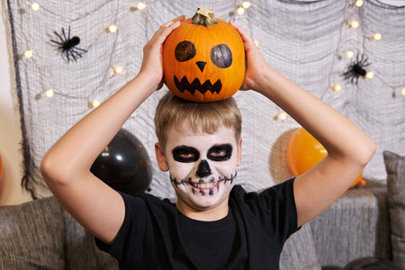 Scary child with a make-up in form of a skeleton and with a pumpkin in his handsの写真素材