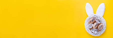 Easter banner with decorative white wreath, quail eggs and rabbit ears on yellow