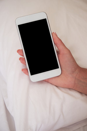 Young woman uses smartphone while lying on bed. Empty smartphone screen. Mocap for mobile appの写真素材