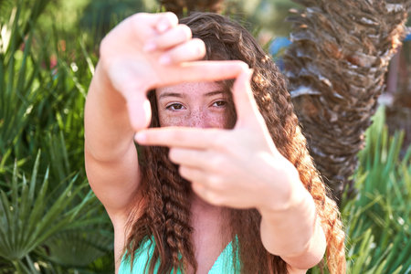 Beautiful teenage girl with freckles and wavy long hair in bathing suit shows frame with her handsの写真素材