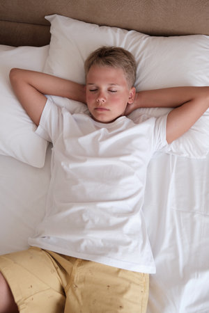 Calm young handsome teenager lies in bed in a white t-shirt in the bedroom at home.の写真素材