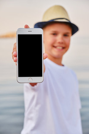 Teenager in straw hat on the seashore demonstrates the screen of a smartphone. Template for design.の写真素材