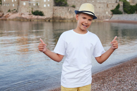 Stylish teen boy on the seashore smiles and points to a white t-shirt.の写真素材