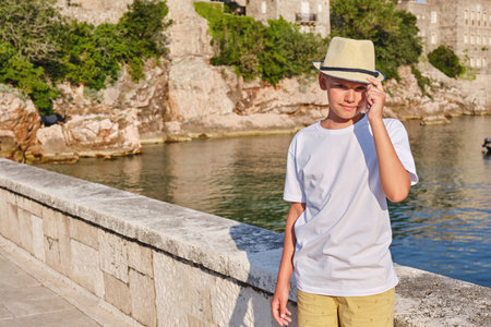 Portrait of a teenager boy in a white t-shirt and straw hat sitting near the sea.の写真素材