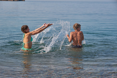 Happy joyful boy and girl swim and splash in sea. Sunny summer day, holiday vacationの写真素材