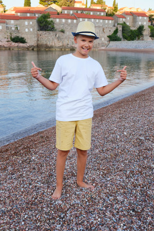 Stylish teen boy on the seashore smiles and points to a white t-shirt.の写真素材