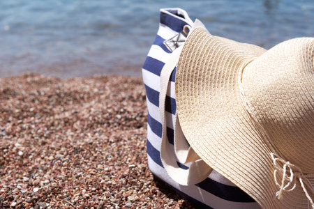 Beach accessories bag and sun hat on pebble beach near the sea. Summer background.の写真素材