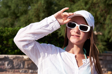 Teen girl with freckles in a white cap with sunglasses on the beach.
