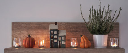 Autumn hygge home decor on shelf in the living room. Decorative house, candles, heather and pumpkin.の写真素材
