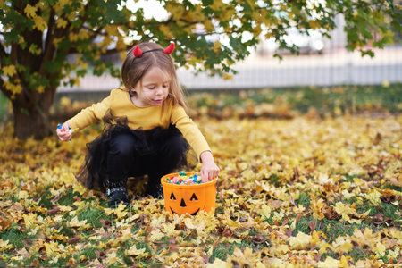 Joyful girl in Halloween costume with a bucket of candies in autumn. trick or treat.の写真素材