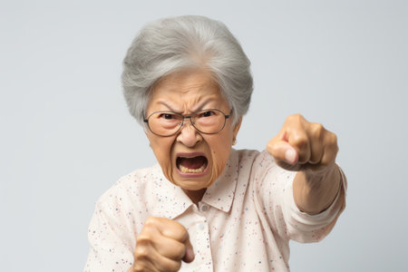 Elderly angry Asian woman frowning and waving her fists indignantly.の素材