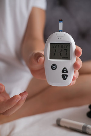 Teenage girl measures blood glucose level on bed at home. Diabetes checking blood sugar level.の写真素材