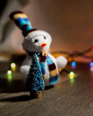 cute Christmas white snowman in a hat and a little Christmas toy tree in the background lights with place for text as substrateの写真素材