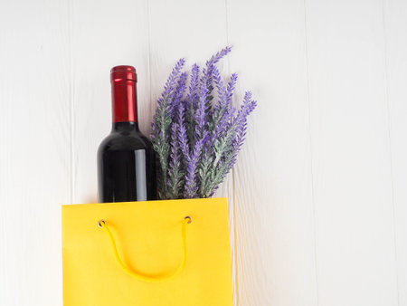 bottle of wine and flowers in the package on wooden background, space for text.