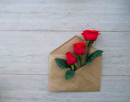 envelope of Kraft paper, with flowers red roses on a wood background, space for text, as congratulation wedding, birthdayの写真素材