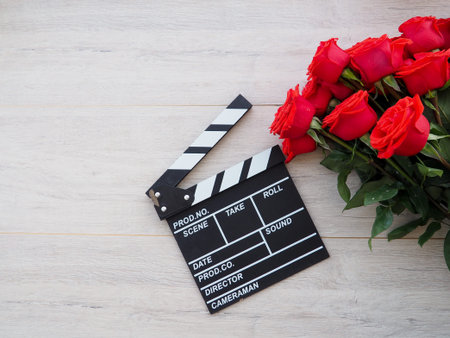 vintage classic clapperboard on brown wooden table whis red roses.