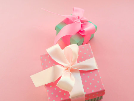 Pink Christmas gift with ribbon, on pink background.