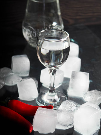 a shot of vodka, an alcoholic beverage, next to ice, fire, ice, red chili pepper. The concept of...