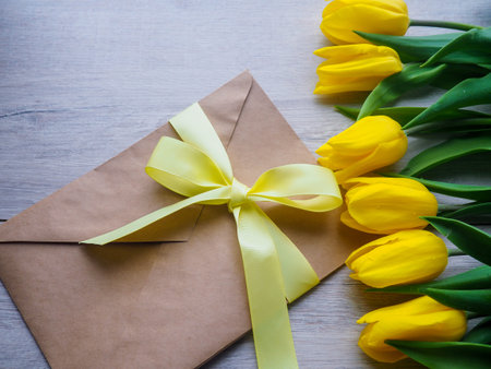 bouquet of yellow tulips on wooden background with envelope, tied with a ribbon space for text.
