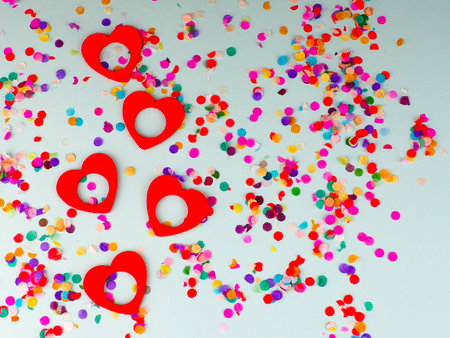 valentine's day, grey background, red hearts with lots of multicolored confetti .