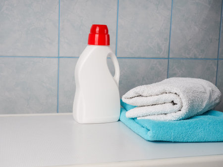 Bottle of detergent and clean towels on washing machine indoors, space for text. Laundry day.