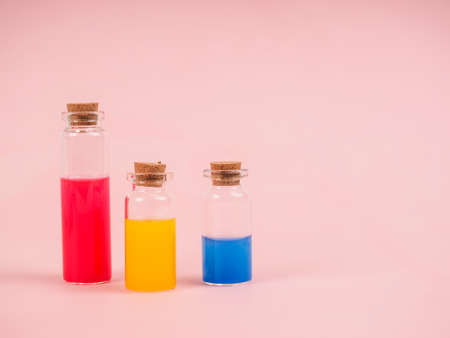Flowers and plant extracts or perfume in small bottles on pink background. three small bubbles with red blue and yellow liquid, the concept of experiments and research. Space for textの写真素材