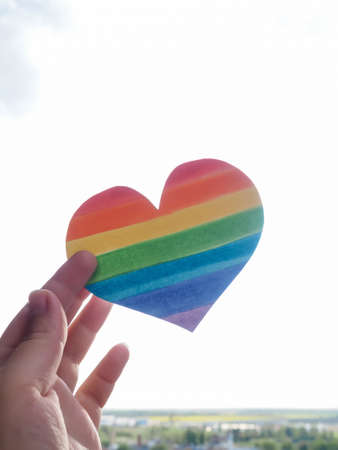 Rainbow Heart, lgbt rights concept, hand holds a heart painted like a LGBT flag, silhouetted against sunの写真素材
