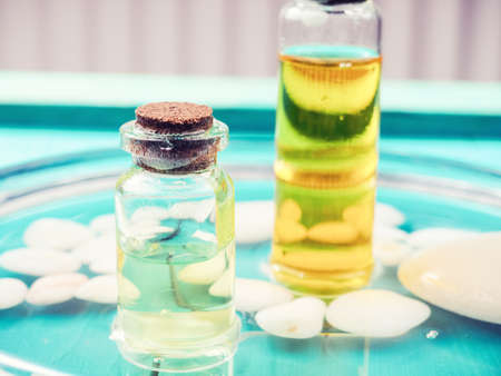Bottle oil cosmetic in clean transparent water with sunlight on blue background. The bottle of Moisturizing cosmetic oil in the water waves on the summer flowers blur backgroundの写真素材