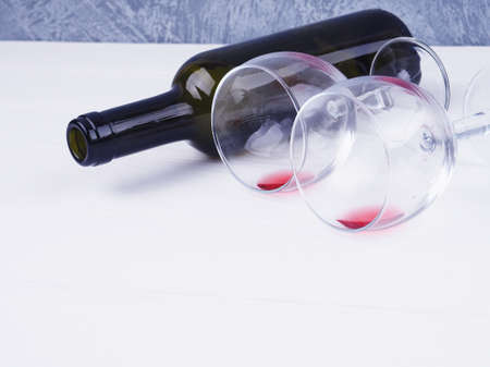 two glasses with leftover wine and a bottle lie on a white background, space for text.の写真素材