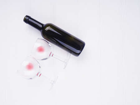 two glasses with leftover wine and a bottle lie on a white background, space for text.の写真素材