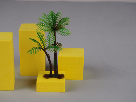 artificial palm tree on yellow cubes on a gray background, colors of the year, design, recreation