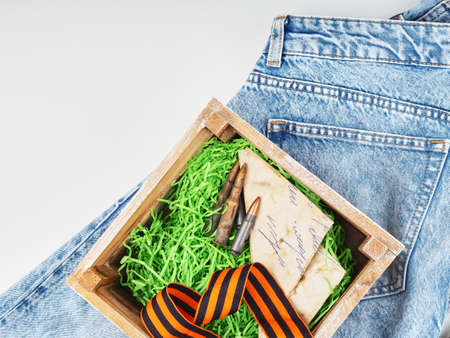 Wooden box inside symbols of mens day, Victory Day, ammunition, letters from the war, stands on modern jeansの写真素材