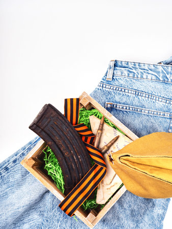 A box with an old magazine for cartridges, cartridges, a St. George ribbon stands on modern jeansの写真素材