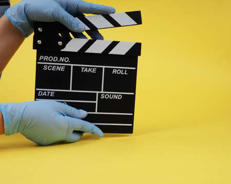 During the period of pandemics, hands in gloves concept of the film industry, a minimalistic composition on a yellow background with glasses and clapperboard. movies and cinemaの写真素材