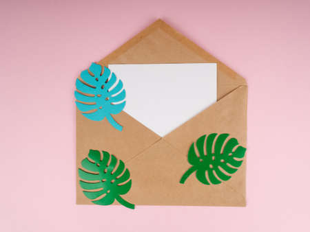 A kraft envelope and a white piece of paper, with monstera paper leaves at the top.の写真素材