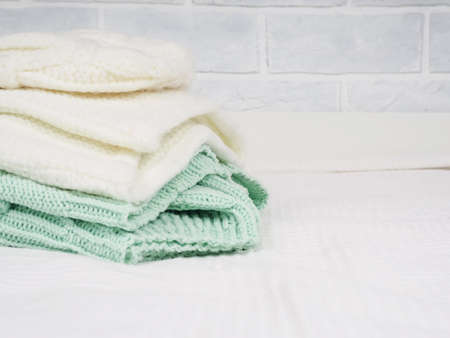 A stack of warm knitted things on a white bed. Cozy clothes. Household concept. folded knitted things whiteの写真素材