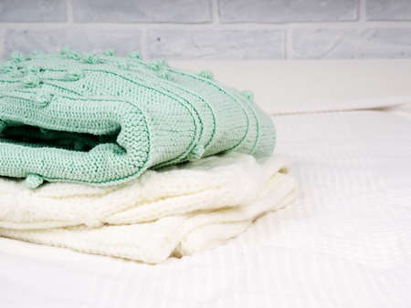 A stack of warm knitted things on a white bed. Cozy clothes. Household concept. folded knitted things whiteの写真素材