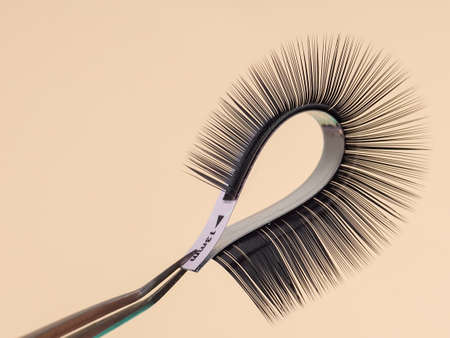 strip for eyelash extensions on a uniform tone, twisted, held with tweezers. Industry artificial eyelashes, eyelash extensions, beautyの写真素材