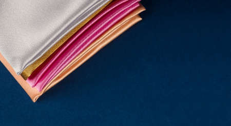 A stack of multi-colored satin fabric on a blue background, space for text.の写真素材