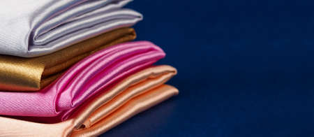 A stack of multi-colored satin fabric on a blue background, space for text.の写真素材