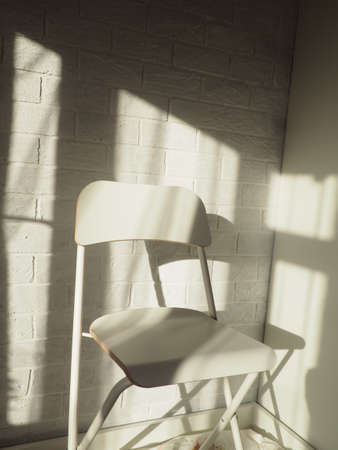 One white chair against a brick wall and light from a window with a shadow.の写真素材