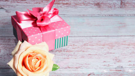 One gift box with a pink bow on a wooden background, copy of the text space one rose nearby.の写真素材